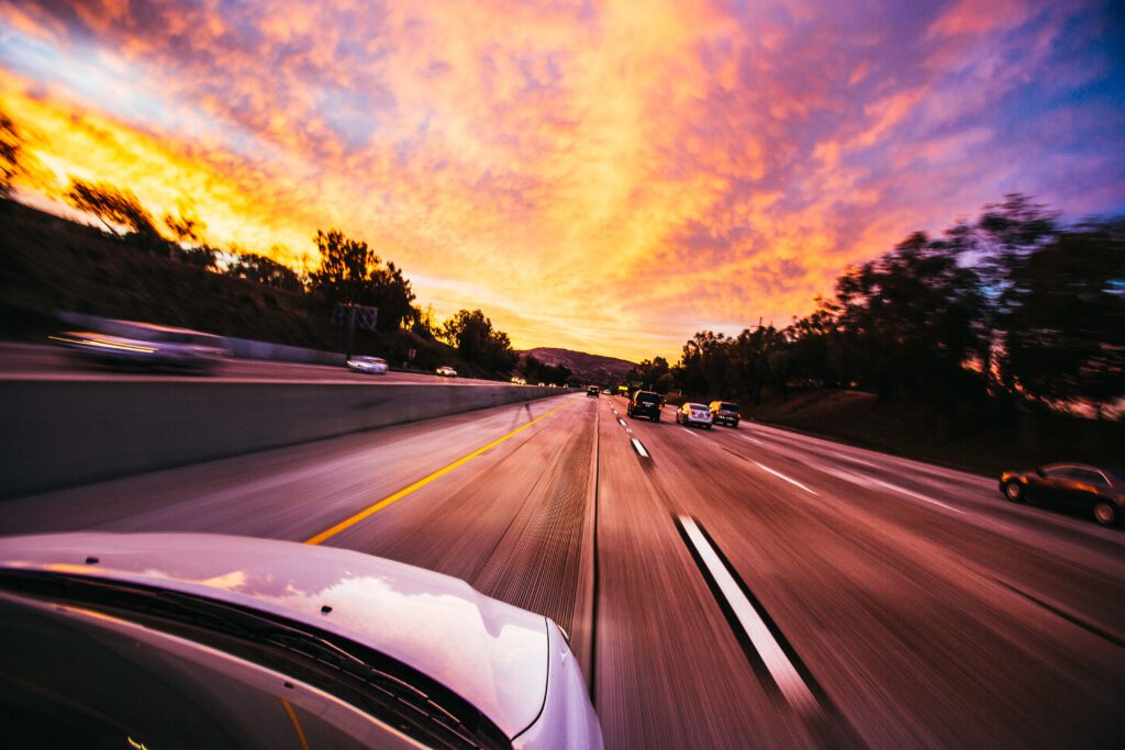 Rijd richting vrijheid met Rijschool Zoetermeer | Go-Buster! Onderga de zonsondergang op de snelweg, jouw witte motorkap kleurt de horizon in blauw, paars en oranje. Start jouw avontuur nu met rijlessen in Zoetermeer!